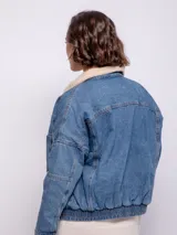 Campera de jean negra con cuello de corderito color crema, cierre frontal con botones metálicos, bolsillos frontales y laterales, y elástico en la cintura.