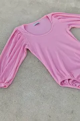 Body de algodón con textura acanalada, color rosado, con escote redondo y mangas largas abullonadas con puños elásticos.