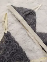 Conjunto de lencería de encaje gris oscuro con detalles en tono marfil, compuesto por un soutien triangular y bombacha a juego.