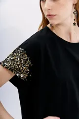 Remera de jersey 100% algodón color blanco, con cuello redondo y manga corta caída. Las mangas están completamente bordadas con lentejuelas tono sobre tono.