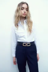Camisa de corte clásico, color blanco, con cuello camisero, cierre frontal de botones y mangas largas con puños abotonados.