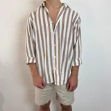 Camisa de lino de corte oversize con diseño de rayas verticales en tonos blanco y tostado, manga larga y cierre frontal con botones.