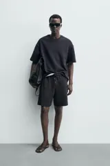 Bermuda estilo jogger de ajuste relajado, color negro, confeccionada en tejido interlock de algodón. Cuenta con cintura elástica ajustable mediante cordón, bolsillos delanteros tipo vivo y diseño liso.