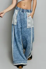 Pantalon de denim azul con lavado vintage, corte ancho y recto, cintura elastizada, grandes bolsillos delanteros de encaje y detalles de ribetes trenzados.