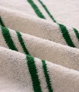 Camisa polo de manga corta confeccionada en tricot texturizado color off-white, con diseño de rayas horizontales verdes y cuello polo verde en contraste. Cuenta con cierre frontal parcial con botones.