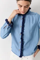 Camisa de jean azul claro con detalles de crochet en color azul oscuro en el cuello, la botonera frontal y los puños. Presenta un corte recto, mangas largas y botones de madera.