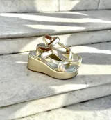 Sandalias de plataforma doradas, con suela ancha y tiras anchas cruzadas en el empeine y una tira ajustable en el tobillo.