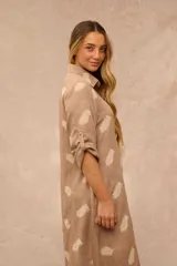 Vestido largo estilo camisero de color beige con estampado de plumas en tono más claro, cuello camisero, botonadura frontal completa, bolsillos laterales y mangas largas con presilla para arremangarlas.