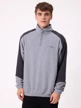 Buzo de polar con cierre frontal parcial, cuello alto y diseño de bloques de color en gris y negro. Presenta logo bordado en el pecho y puños elásticos.