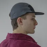 Gorro estilo five-panel de nylon, bicolor, con paneles superiores grises y panel frontal y visera negros. Presenta un parche rectangular negro con el logo 'PULAU' en blanco.