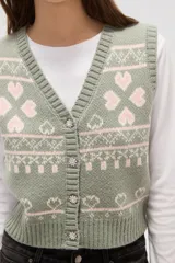 Chaleco tejido de punto con diseño jacquard de corazones y motivos geométricos en tonos verde y rosa. Presenta escote en V, cierre frontal con botones y terminaciones acanaladas en cuello, sisas y ruedo.