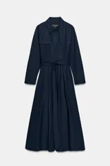 Vestido midi de estilo camisero en color azul marino, con cuello solapa, cierre frontal de botones ocultos y manga larga. Presenta bolsillos laterales, solapas decorativas en el pecho y un cinturón de lazada en el mismo tejido para ajustar la cintura.