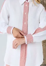 Camisa de lino blanca de corte relajado, con cuello camisero, manga larga y detalles a rayas rojas en la botonera frontal, los puños y los hombros.