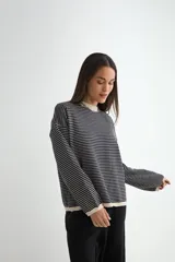 Buzo de punto con diseño a rayas horizontales finas, cuello redondo y puños en color negro. Presenta un corte holgado y mangas largas.