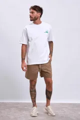 Remera blanca de manga corta con un pequeño estampado verde en el pecho que simula una caja abierta con un objeto dentro.