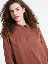 Vestido camisero largo color marrón con sutil estampado geométrico en relieve, de manga larga con terminación acampanada, cuello camisero y cierre frontal de botones.
