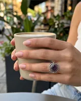Anillo de plata 925 con piedra amatista central de corte circular, rodeada por un diseño de pequeñas esferas metálicas.