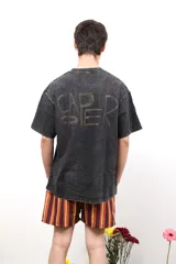 Remera de algodón con efecto lavado ácido en color negro, de corte holgado y manga corta. Presenta un estampado artístico en color rojo en la parte posterior con la palabra Caper.