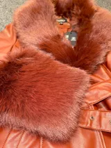 Tapado de cuero sintético color bordó, con cuello y puños de piel sintética desmontables. Presenta cierre frontal con botones y cinturón ajustable con hebilla forrada en el mismo material.