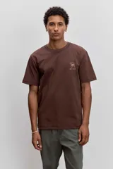 Remera de algodón color marrón chocolate, de corte clásico y cuello redondo, con un pequeño estampado gráfico en el pecho.