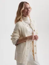 Cárdigan largo color crema, confeccionado en tejido de punto acanalado de viscosa. Tiene corte relajado, cierre frontal con botones y bolsillos de parche.