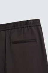 Pantalón regular fit color marrón oscuro, confeccionado en tejido con viscosa. Cuenta con cintura elástica, bolsillos delanteros y detalle de bolsillos traseros de vivo. El cierre frontal es con cremallera y botón.