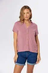 Camisa lisa de lino color beige, de manga corta, con cuello camisero, bolsillo ojal en el pecho y cierre frontal con botones.