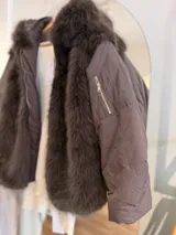 Campera puffer oversize color marrón, con paneles frontales y traseros de pelo sintético suave. Presenta mangas acolchadas, cierre frontal y bolsillo con cierre en la manga.