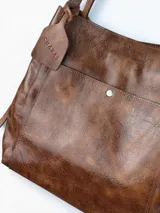 Bolso tipo tote grande de cuero genuino marrón, con asas de hombro dobles, bolsillo exterior con botón a presión y llavero colgante con la marca grabada.