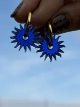 Par de dijes colgantes con forma de sol, realizados en acrílico color azul vibrante, diseñados para ser utilizados en aros tipo argolla.