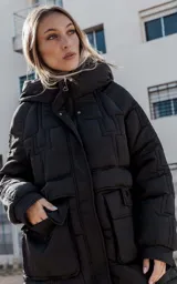 Campera larga acolchonada color marrón, con diseño midi, capucha amplia, cierre frontal con cremallera y broches, y bolsillos delanteros con tapa.
