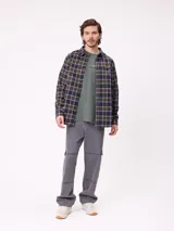 Camisa de manga larga con estampado de cuadros en tonos blanco, gris y azul. Presenta cuello clásico, cierre frontal con botones y un pequeño parche con logo en el pecho.