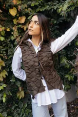 Chaleco de tweed marrón con textura, presenta un diseño frontal con volados estructurados y cordones decorativos en zigzag. Cuenta con cierre frontal mediante lazos ajustables.