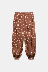 Pantalón de tiro medio con diseño bombacho, confeccionado en tejido satinado con estampado de manchas abstractas. Presenta bolsillos delanteros, cierre lateral con cremallera oculta y bajos terminados en puño con botón.