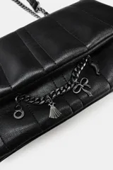 Bolso bandolera de diseño acolchado en color negro, con solapa frontal decorada con una cadena metálica y charms colgantes. Cuenta con cierre de botón imantado, triple compartimento interior y correa ajustable que permite llevarlo al hombro o cruzado.
