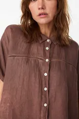 Camisa de lino color azul, de corte holgado, mangas cortas, cuello camisero y cierre frontal con botones. Presenta detalles de calados horizontales en el pecho.