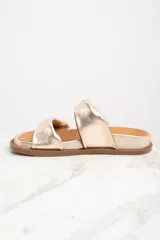 Sandalias bajas con base dorada y dos tiras anchas cruzadas en cuero color marrón y dorado.