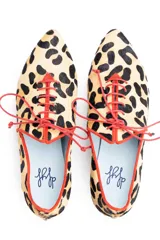 Zapatos tipo blucher de pelo de pony con estampado animal print. Presentan cierre de cordones rojos, ribetes de ante a contraste y una silueta geométrica con aberturas laterales. Cuentan con tacón forrado de 2 cm en forma de lágrima y suela de cuero.