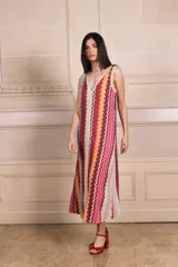 Vestido largo sin mangas de tejido de punto con diseño de rayas verticales en zigzag multicolor. Presenta escote en V profundo tanto en el frente como en la espalda, con detalles de vivos en color crema y acabado con sutil brillo.