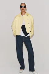 Chaqueta corta confeccionada en mezcla de algodón color amarillo claro, con cuello de solapa, manga larga, bolsillos delanteros y cierre frontal con botones visibles en los extremos.