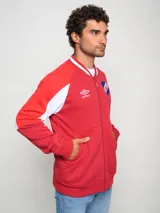 Campera tipo bomber de felpa, color rojo con detalles en blanco en las mangas y cuello. Presenta cierre frontal completo, logo de Umbro y escudo del Club Nacional de Football bordados en el pecho.