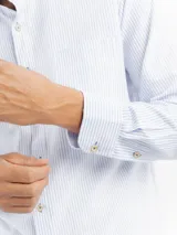 Camisa de manga larga con diseño de rayas finas, cuello con botones y bolsillo frontal. Presenta cierre de botonadura frontal y corte regular.