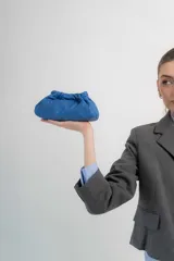 Cartera tipo sobre de cuero color azul, con diseño fruncido en la parte superior y costuras pespunteadas visibles.