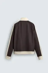 Sudadera de corte relajado en color azul marino con cuello alto y cierre frontal de cremallera. Presenta bandas laterales en color crema a contraste que recorren las mangas, puños y bajo en tejido rib, y bolsillos laterales de vivo.