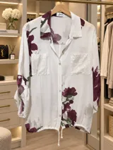Camisa blanca de manga larga con estampado floral en tonos bordó y verde, cuello camisero, cierre frontal de botones y bolsillos en el pecho con apliques de lentejuelas.