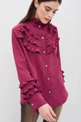 Camisa de manga larga en color rosado, con diseño de volados en cascada en el frente y en los puños. Presenta cuello alto con terminación suave y cierre frontal con botones.
