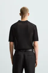 Polo de manga corta color negro, con cuello solapa y cierre frontal de botones. Confeccionado en tejido de punto con estructura abierta y calada.
