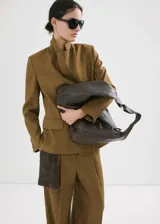 Blazer de lino color verde militar, de corte recto y diseño estructurado, con cuello en pico y solapas de muesca. Presenta mangas largas con puños abotonados, bolsillos con solapa en la parte delantera y cierre frontal de botonadura doble con abertura posterior en el bajo.