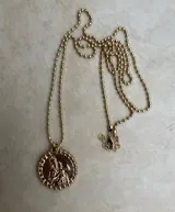 Collar dorado con cadena de bolitas y dije redondo con diseño de figuras religiosas.