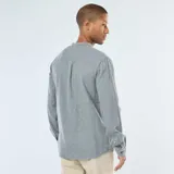 Camisa de manga larga color gris jaspeado, confeccionada en tejido de franela. Presenta cuello mao (o cuello mandarín) y cierre frontal de botones marrones. Incluye un bolsillo de parche en el pecho izquierdo.